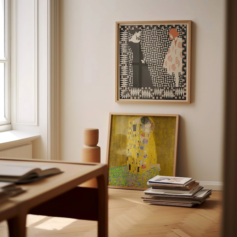 May include: Two square framed art prints. The top print features two figures in black and white with geometric patterns. The bottom print displays a golden, yellow-toned painting of two figures embracing amidst a field of colourful floral patterns.