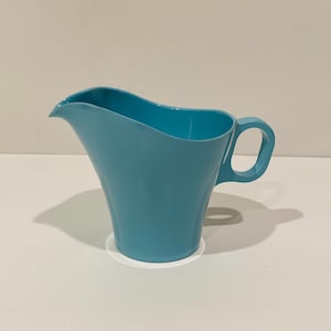 May include: A light blue plastic pitcher with a curved handle. The pitcher is sitting on a white surface.