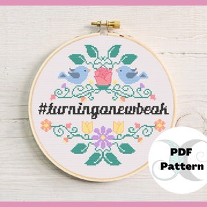 May include: A cross-stitch embroidery hoop featuring a floral design with two blue birds, a pink rose, and the text "#turninganewbeak". The design is surrounded by a wooden hoop and includes a "PDF Pattern" graphic.