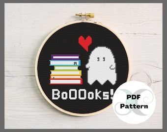 May include: A black and white cross stitch pattern of a ghost holding a stack of books with a red heart above the ghost. The text "Booooks!" is below the ghost. The pattern is in a round embroidery hoop.
