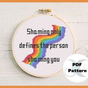 May include: A cross-stitch pattern featuring a rainbow with the text "Shaming only defines the person shaming you". The pattern is in a white embroidery hoop and includes a PDF pattern label.