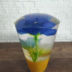 May include: A clear glass sphere with a blue flower inside. The sphere is on a yellow base.