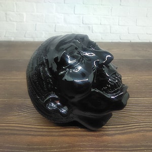 Peut inclure: Une tête sculptée noire et brillante avec un visage détaillé et un dessus texturé. La tête est inclinée sur le côté et la bouche est légèrement ouverte.