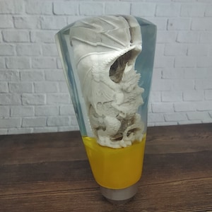 Op de afbeelding: Een transparante resin versnellingspookknop met een wit drakenbeeldje erin. De basis van de knop is geel.