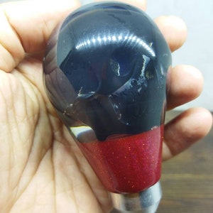 Op de afbeelding: Zwarte en rode hars versnellingspookknop met een zilveren basis. De bovenkant van de knop is zwart en de onderkant is rood met glitter.