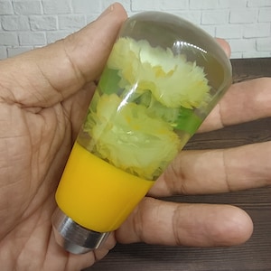 May include: A yellow and clear resin gear shift knob with white flowers inside. The knob has a silver base.