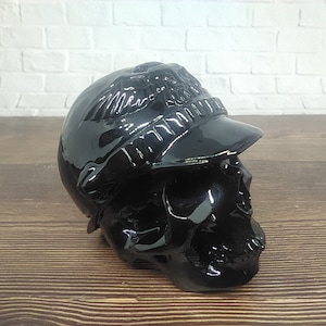 May include: Black skull figurine wearing a black cap. The cap features a raised eagle design and the text "Harley Davidson" on the front.