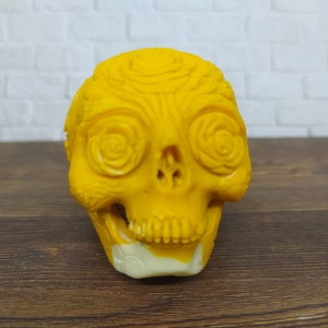 Peut inclure: Un crâne en céramique jaune avec un motif floral détaillé. Le crâne a une mâchoire inférieure blanche et est décoré de volutes et de roses complexes.