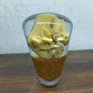 Op de afbeelding: Een transparante hars schakelknop met een gouden glitterbasis en een goudkleurig object erin.