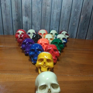 May include: A set of 15 colorful skull-shaped billiard balls arranged in a triangle formation on a wooden surface. The balls are painted in various colors, including red, yellow, blue, green, and orange.