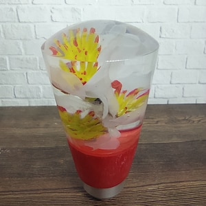 Könnte beinhalten: Ein transparenter Glasschaltknauf mit roter Basis und gelben und roten Blumen im Inneren.