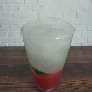 May include: A tall glass filled with ice and a red smoothie. The glass is on a wooden surface.