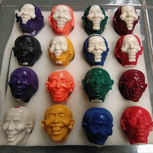 Puede incluir: Una colección de 15 figuritas de cerámica pintadas a mano, con rostros humanos. Las figuritas son de diferentes colores y tienen diferentes expresiones faciales. Están dispuestas en una cuadrícula sobre una superficie blanca.