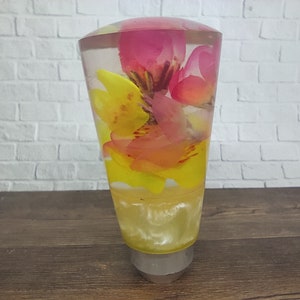 May include: A clear glass gear shift knob with pink and yellow flowers encased inside. The flowers are arranged in a cluster and appear to be floating in the clear liquid.
