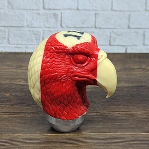 May include: A decorative eagle head sculpture, featuring a red and cream color scheme. The eagle's head is detailed with a cream-colored beak and a base. The number "11" is visible on the top of the head.