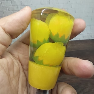 Könnte beinhalten: Ein gelber Schaltknauf aus Harz mit einer durchsichtigen Harzoberseite, die drei gelbe Zitronen enthält. Die Zitronen sind von grünen Blättern umgeben.