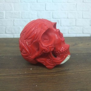 Peut inclure: Une sculpture de crâne rouge avec des sculptures complexes. Le crâne est fait d'un matériau lisse et poli et présente un design détaillé.