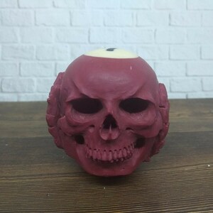 Puede incluir: Un cráneo rojo con forma de bola de billar con un número uno blanco en la parte superior.