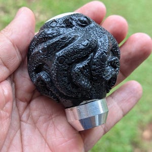 Op de afbeelding: Een witte keramische mok met een zwart handvat en de tekst "But First, Coffee" in een zwarte, handgeschreven lettertype. De mok staat op een wit oppervlak.