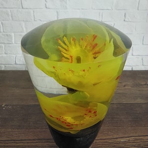 Op de afbeelding: Een heldere glazen kegel met een gele bloem erin. De bloem heeft rode accenten en is van alle kanten zichtbaar.