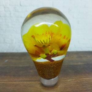May include: A clear glass gear shift knob with a yellow flower inside and gold glitter around the base.