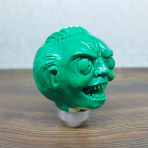 May include: Green plastic figurine of a creature with a menacing expression. The creature has large eyes, sharp teeth, and a detailed face.