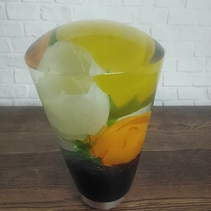 Könnte beinhalten: Eine klare Glasvase mit einem gelben, orangen und weißen Blumendesign. Die Vase hat die Form eines Kegels und eine abgerundete Oberseite.