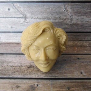 Peut inclure: Un buste en ivoire sculpté d'une personne aux cheveux courts et ondulés. Le buste est de couleur crème clair et présente un visage détaillé avec un léger sourire.