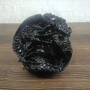 May include: A black, detailed, resin sculpture of a dragon's head. The sculpture is highly textured and has a glossy finish.