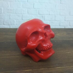 Puede incluir: Un objeto rojo con forma de cráneo con un número 8 blanco en la parte superior de la cabeza. El cráneo está hecho de un material liso y brillante.