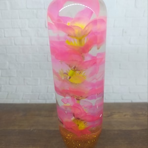 Pode incluir: Uma alavanca de câmbio de resina transparente rosa e dourada com flores cor-de-rosa no seu interior. A alavanca tem uma base de glitter dourado.