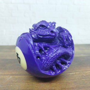 Peut inclure: Une boule de billard violette avec un motif de dragon sculpté sur la surface. La boule porte le numéro "7" en blanc.