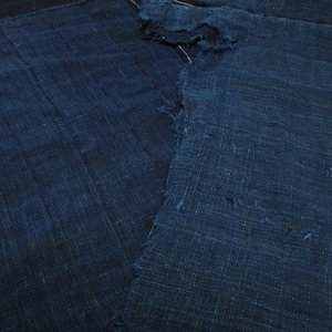 Puede incluir: Un trozo de tela azul índigo oscuro con una textura tejida visible y bordes deshilachados. El tejido muestra un color profundo y saturado con variaciones sutiles de tono en toda la superficie, presentando un patrón de tejido rústico y grueso.