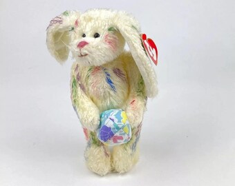 May include: White plush bunny with colorful paint splatter design holding a small, colorful Easter egg. The bunny has a red Beanie Baby tag attached to its ear.