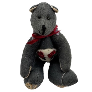 May include: A gray teddy bear with a red ribbon around its neck and a white patch on its belly decorated with red roses. The bear has small, round ears and a black nose.