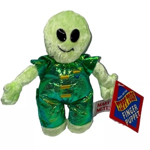 Op de afbeelding: Groene alien-vingerpppetje met een groen en gouden pakje. De pop heeft grote zwarte ogen en een brede glimlach. Het label vermeldt "Tippy Toes Finger Puppet" en "Mary Meyer".