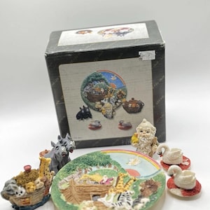 Puede incluir: Un juego de té en miniatura del Arca de Noé con un plato colorido que representa el arca con animales, una tetera con forma de arca, una jarra de crema con forma de cisne, un azucarero con forma de gnomo y dos tazas de té con forma de cisnes.