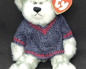 May include: A plush teddy bear with gray and white fur, wearing a blue knit sweater with red accents. The bear has a black nose and a red heart-shaped tag.