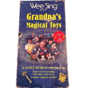 May include: A vintage VHS tape for "Wee Sing Presents Grandma's Magical Toys." The cover is dark blue with yellow text and features a photo of children and an older man. Includes the text "A Lively Musical Adventure."
