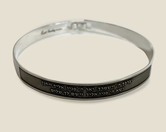May include: A silver bangle bracelet with a black band engraved with Hebrew text. The text reads: "Yivrakha Hashem veyishmerekha. Ya'er Hashem panav elekha veyichaneka. Yisa Hashem panav elekha veyasem lekha shalom."