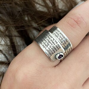 Puede incluir: Un anillo de plata con una piedra morada engastada en el centro. El anillo está grabado con texto hebreo.