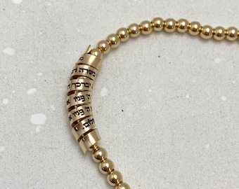 May include: A gold bracelet with a charm that has Hebrew writing on it.