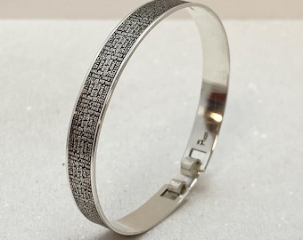 May include: A silver bangle bracelet with a Hebrew inscription engraved around the band. The bracelet has a hinged clasp.