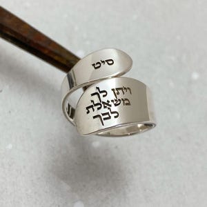 May include: A silver ring with Hebrew text engraved on it. The text reads "Shema Yisrael" and "Adonai Eloheinu Adonai Echad" on one side and "Shalom" on the other side.