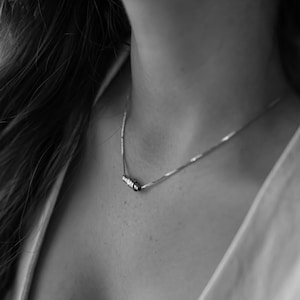 May include: A silver chain necklace with a small, rectangular pendant. The pendant has a row of small, clear stones.
