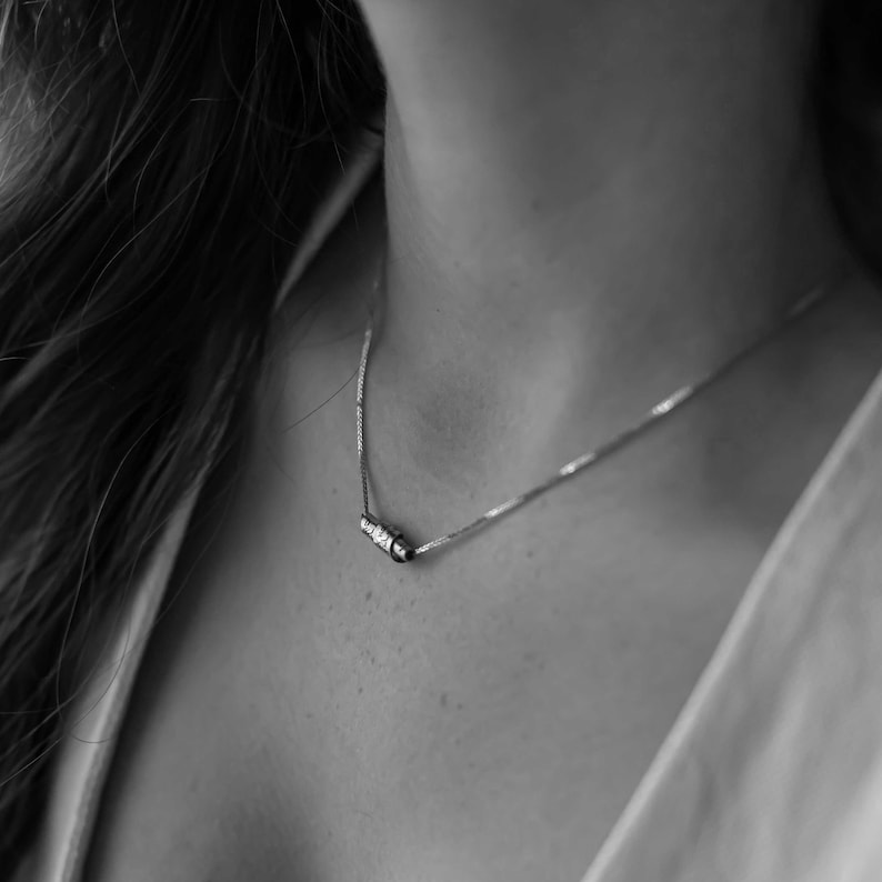 May include: A silver chain necklace with a small, rectangular pendant. The pendant has a row of small, clear stones.