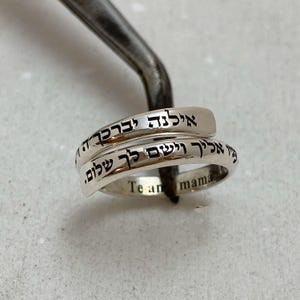 May include: A silver ring with two bands, one inscribed with Hebrew text and the other with the words "Te amo mama".