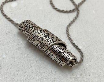 Puede incluir: Collar de plata con un colgante hecho de varios anillos de plata, cada uno grabado con texto hebreo.