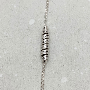 May include: A silver chain necklace with a silver charm that has Hebrew text engraved on it.