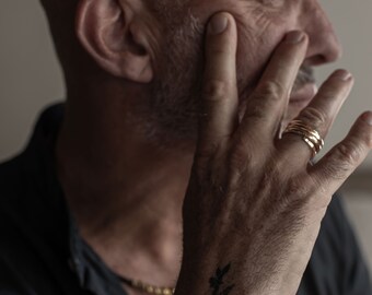 May include: A close-up of a person's hand wearing multiple thin gold bands. The hand is resting on the person's cheek, and the person's face is partially visible in the background.